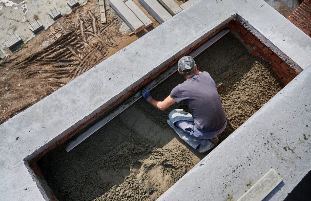Top view of male contractor placing screed rail on the floor covered with sand-cement mix at construction site. Man worker leveling surface with straight edge while screeding floor in new building.