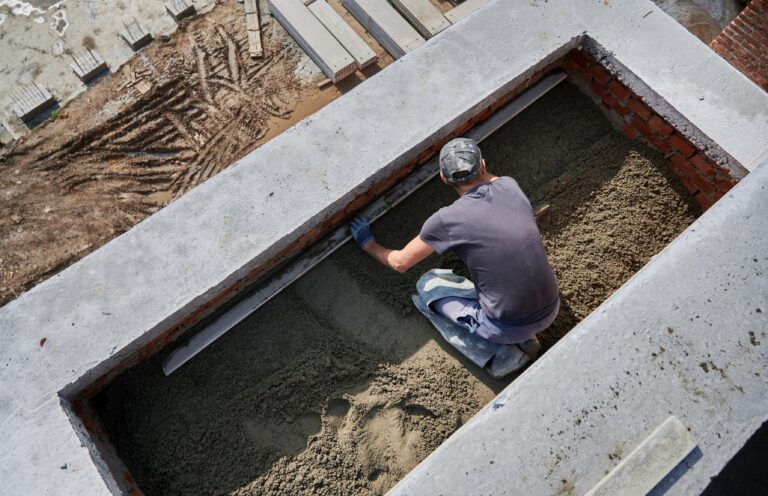 Top view of male contractor placing screed rail on the floor covered with sand-cement mix at construction site. Man worker leveling surface with straight edge while screeding floor in new building.